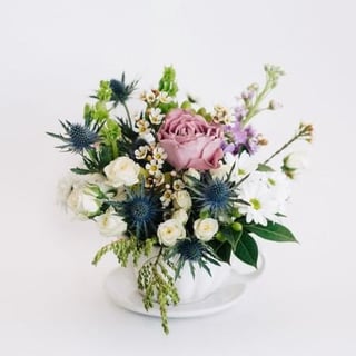 White teacup arrangement featuring blue, white and lilacs with roses, seaholly, chrysanthemums, stock and waxflower. Melbourne delivery only.