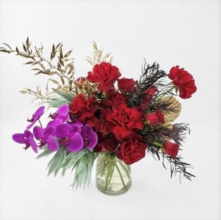 Luxurious vase arrangement of 24 red roses with magenta phalaenopsis stem in vase.