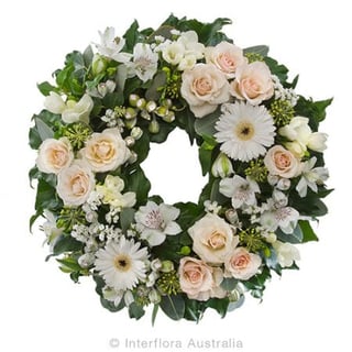 Serenity - soft pinky peach spray roses mini white gerberas and white alstromeria funeral wreath. Melbourne and Australia wide delivery with Interflora Flowers.
