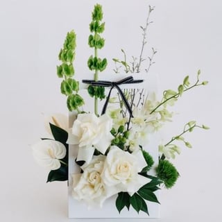 Vamos - white carry box flower arrangement featuring white reflexed roses, molucca balm, green trix and white singapore orchids.