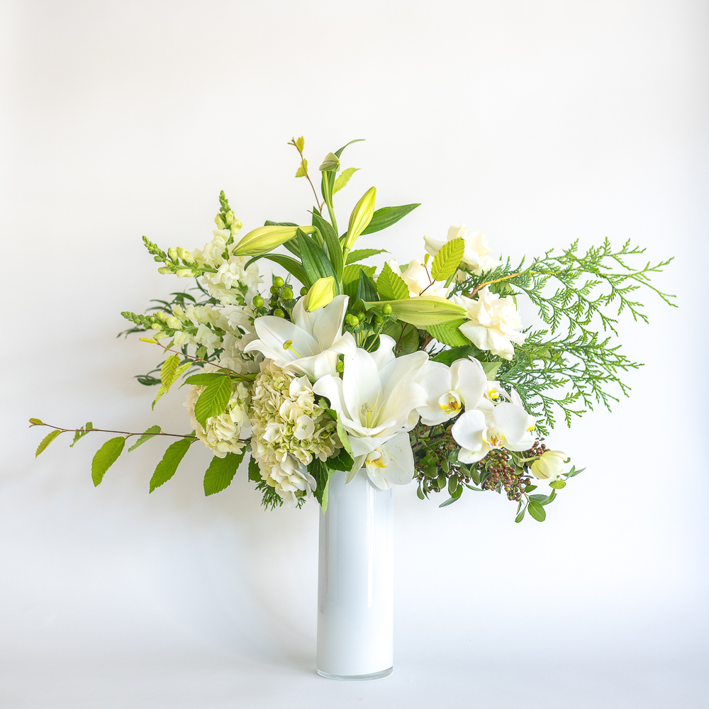Premium white Christmas bouquet in vase arrangement featuring white november lilies, green trix, snapdragons, hydrangea, roses, phalaenopsis orchdis.