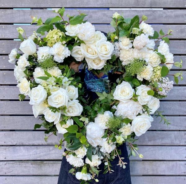 White wreath featuring white roses, carnations, queen annes lace, and seasonals to compliment.